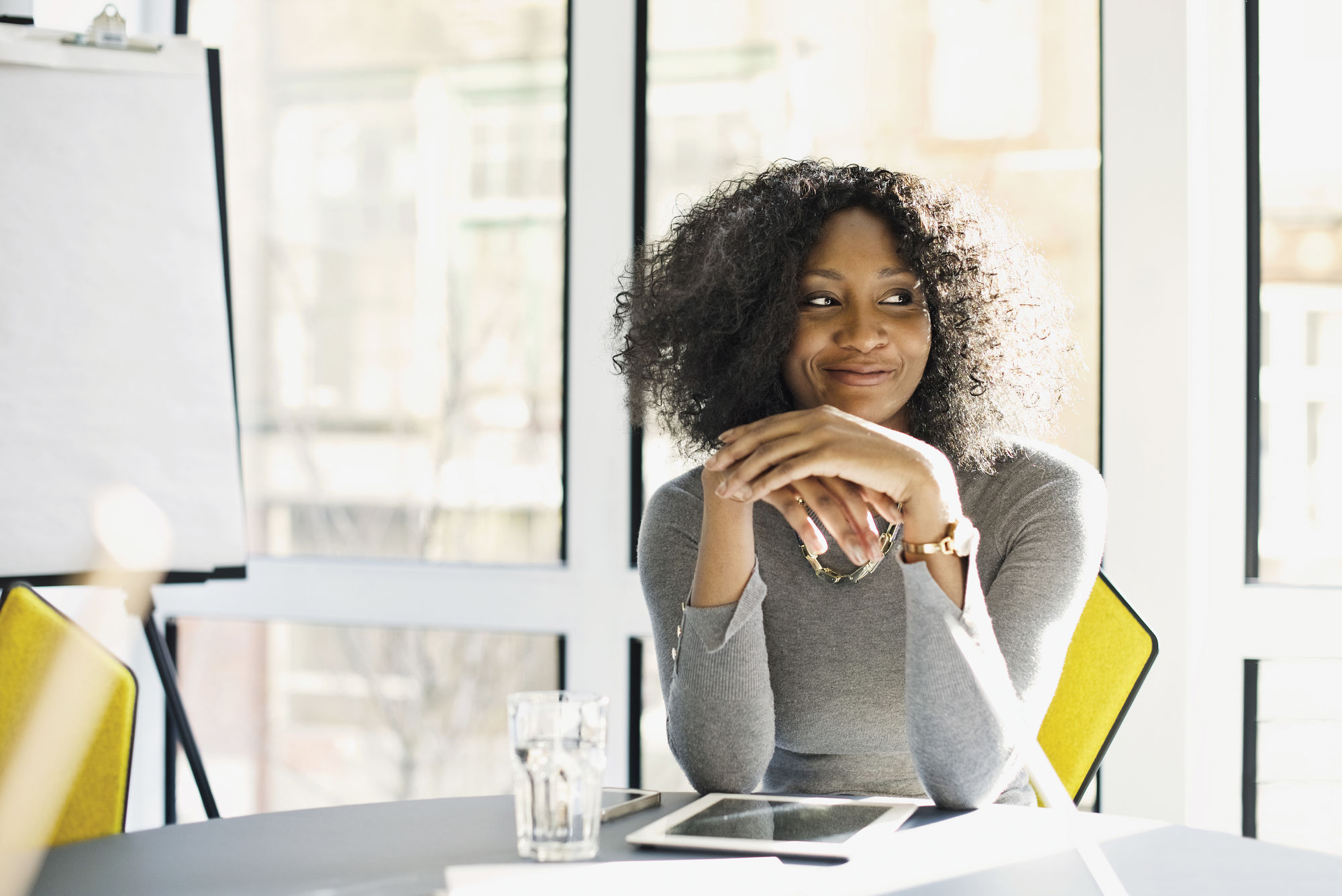 Young business woman sitting at a table in a meeting room, smiling. Flip-Chart and bright windows.